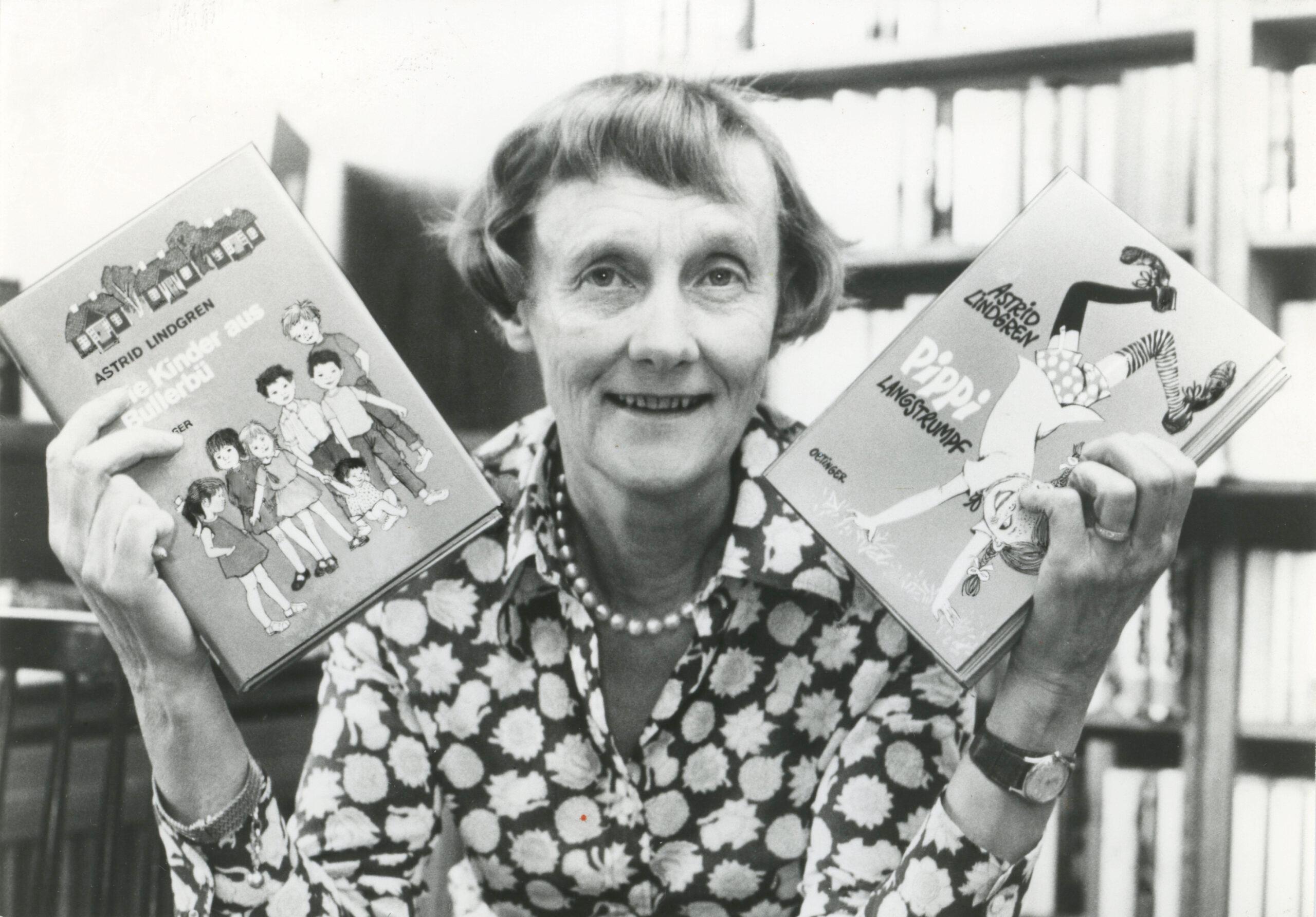 A black-and-white photo of Astrid Lindgren holding one Pippi Longstocking book in each hand.