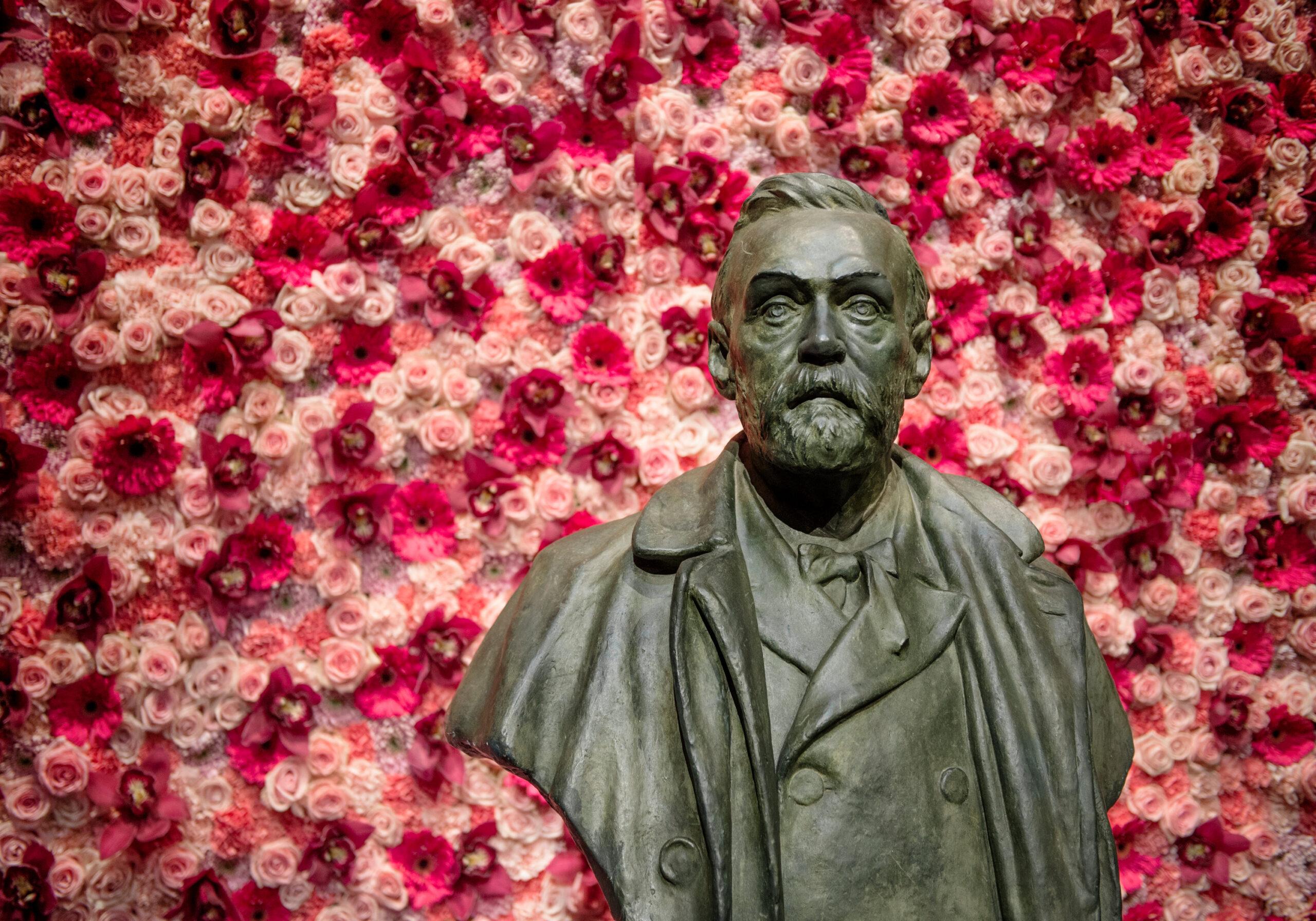 A bust of Alfred Nobel in front of a wall of flowers.