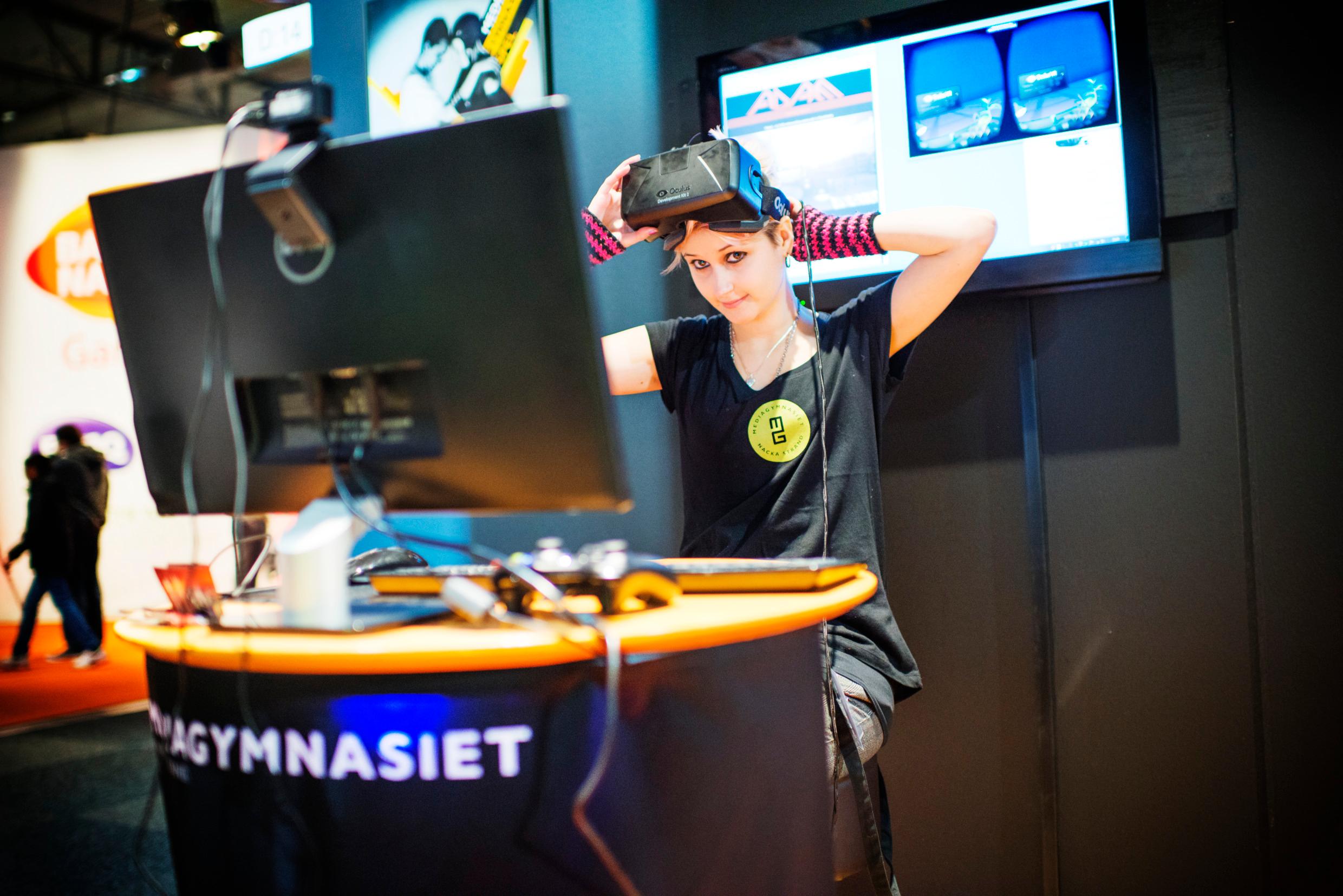 A woman sitting in front of a big computer screen with a VR headset on her head.