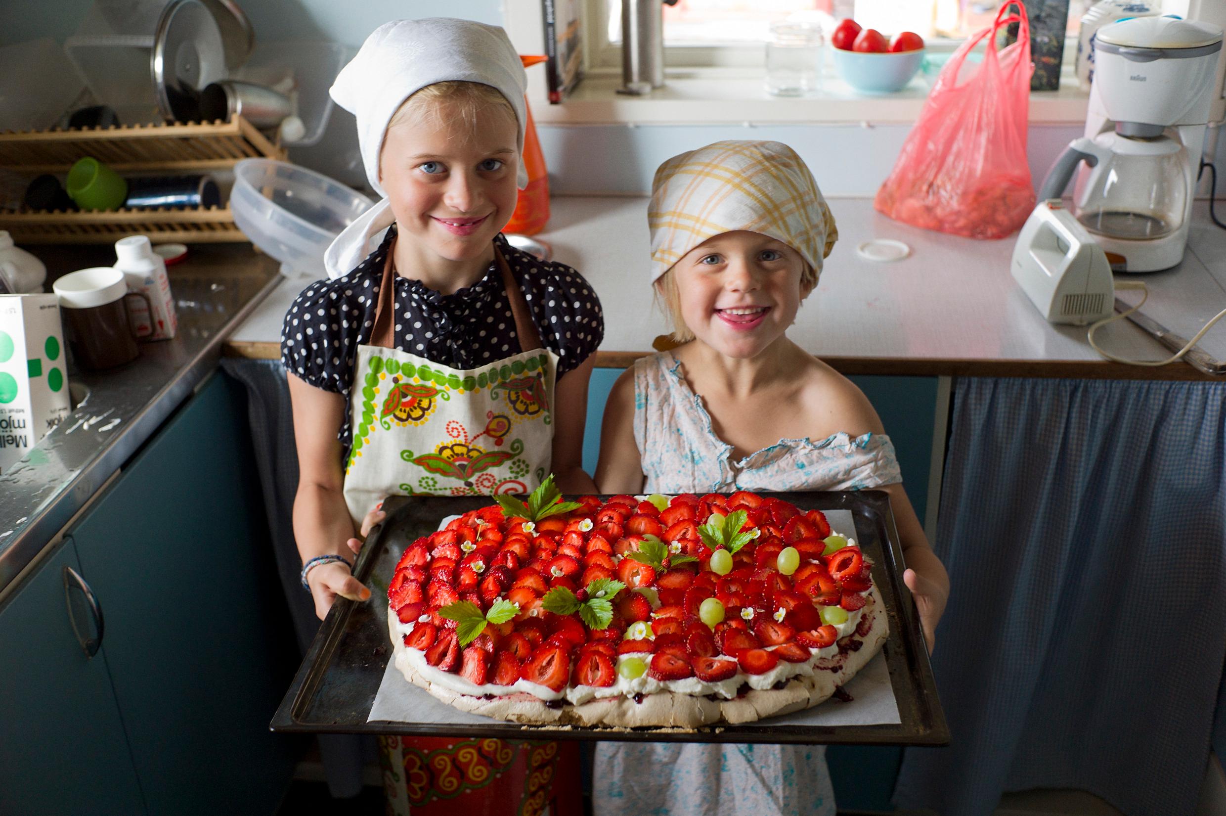 Two girls with headscarves and aprons holding a strawberry cake – one of many classic Swedish recipes.