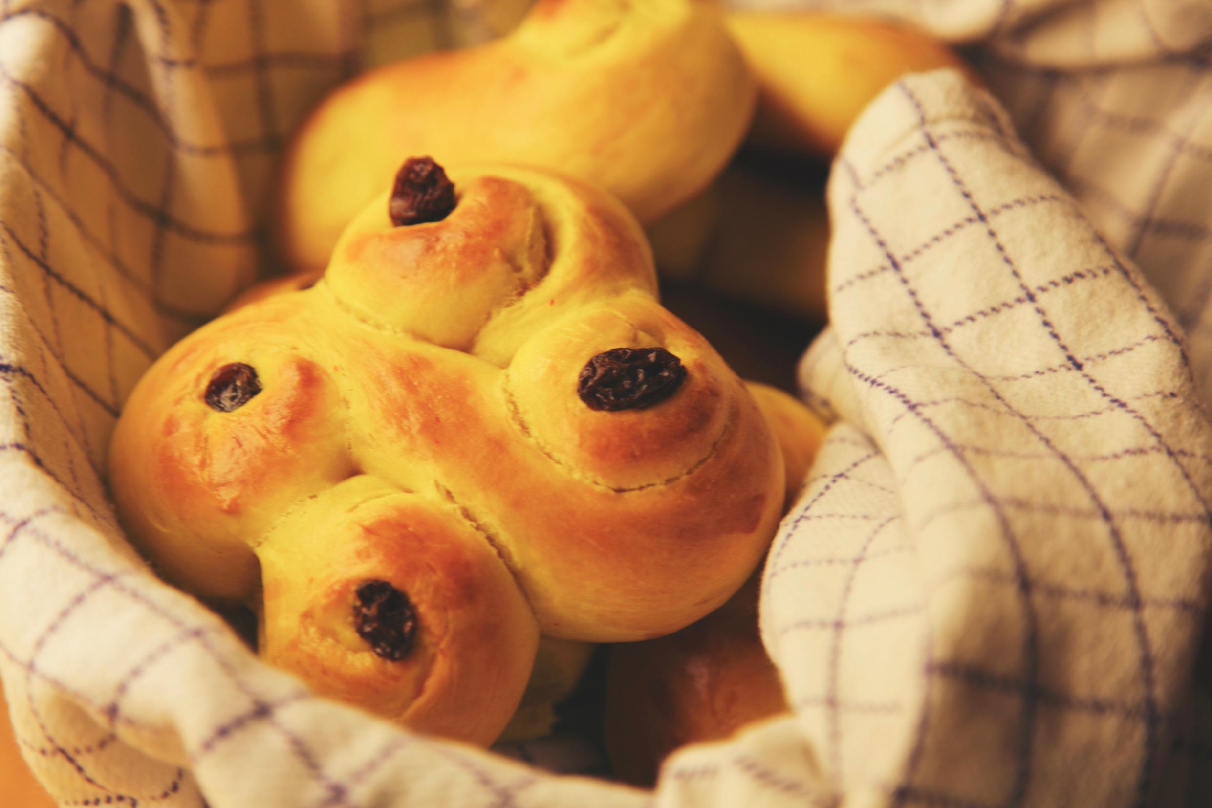 A basket with yellow saffron buns topped with raisins. The buns are a square made up of two intertwined eights.