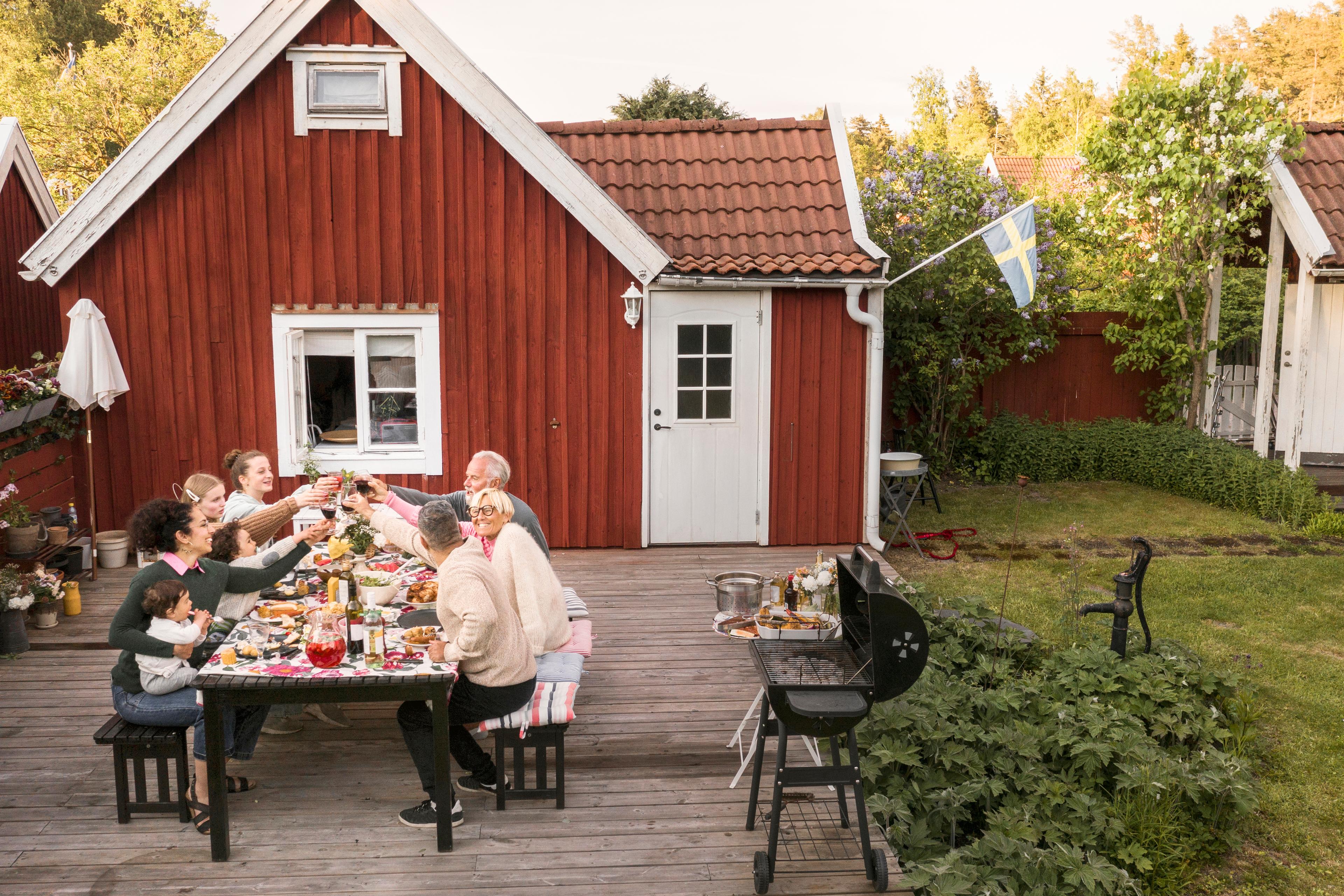 People sitting at an outdoor table in front of a house, eating and drinking.