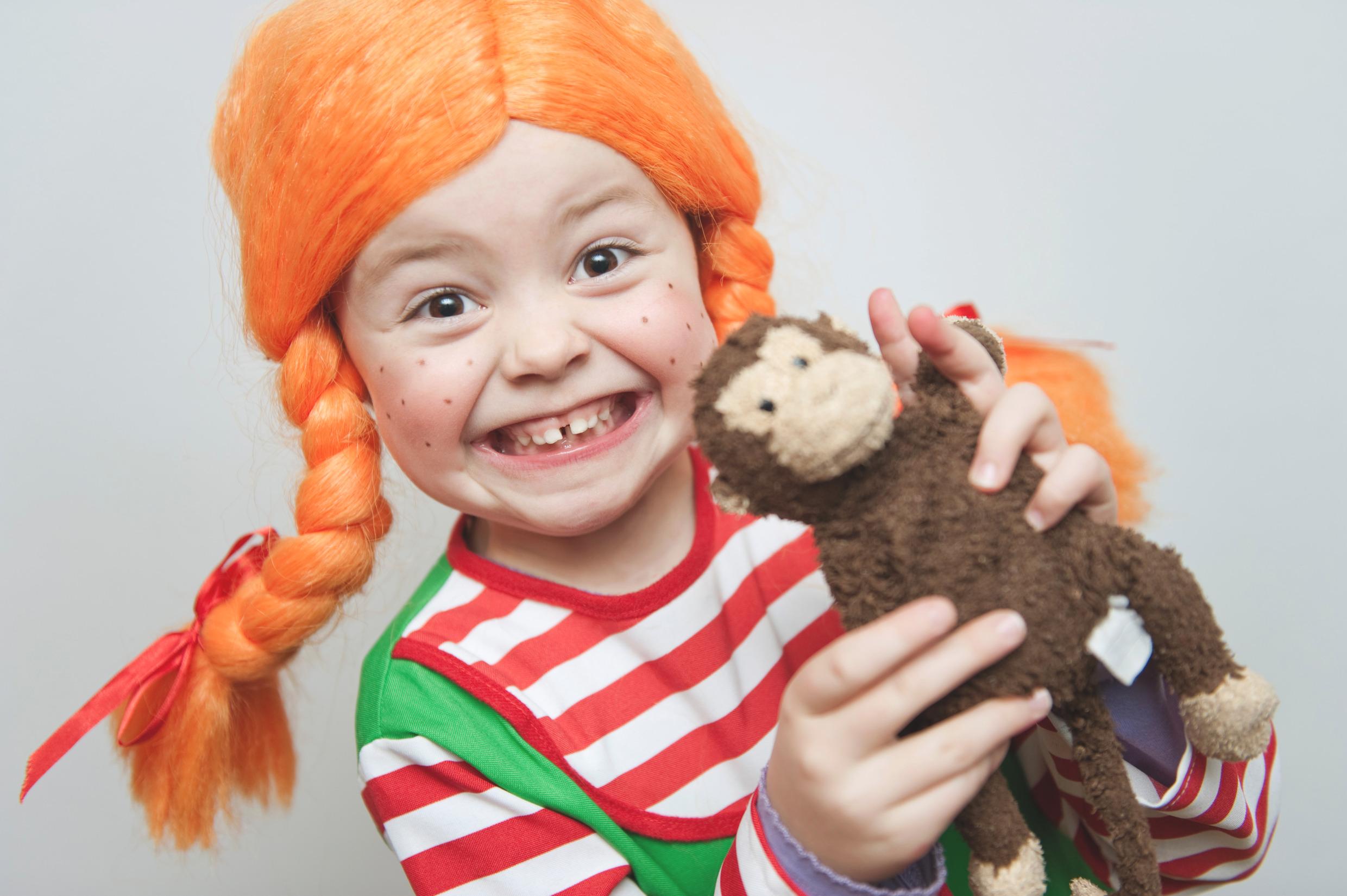 A child dressed up as Pippi with a wig holds a monkey.